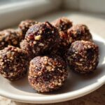 A cluster of rich, dark No Bake Pecan Pie Balls coated in chopped nuts, resting on a white plate in natural light.