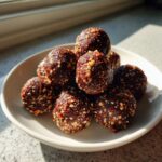 A stack of rich, dark No Bake Pecan Pie Balls coated in chopped nuts, sitting on a white plate in natural light.