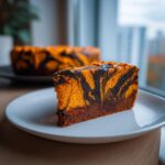 A slice of Orange And Black Halloween Marble Cake showing vibrant orange and dark swirls on a white plate.