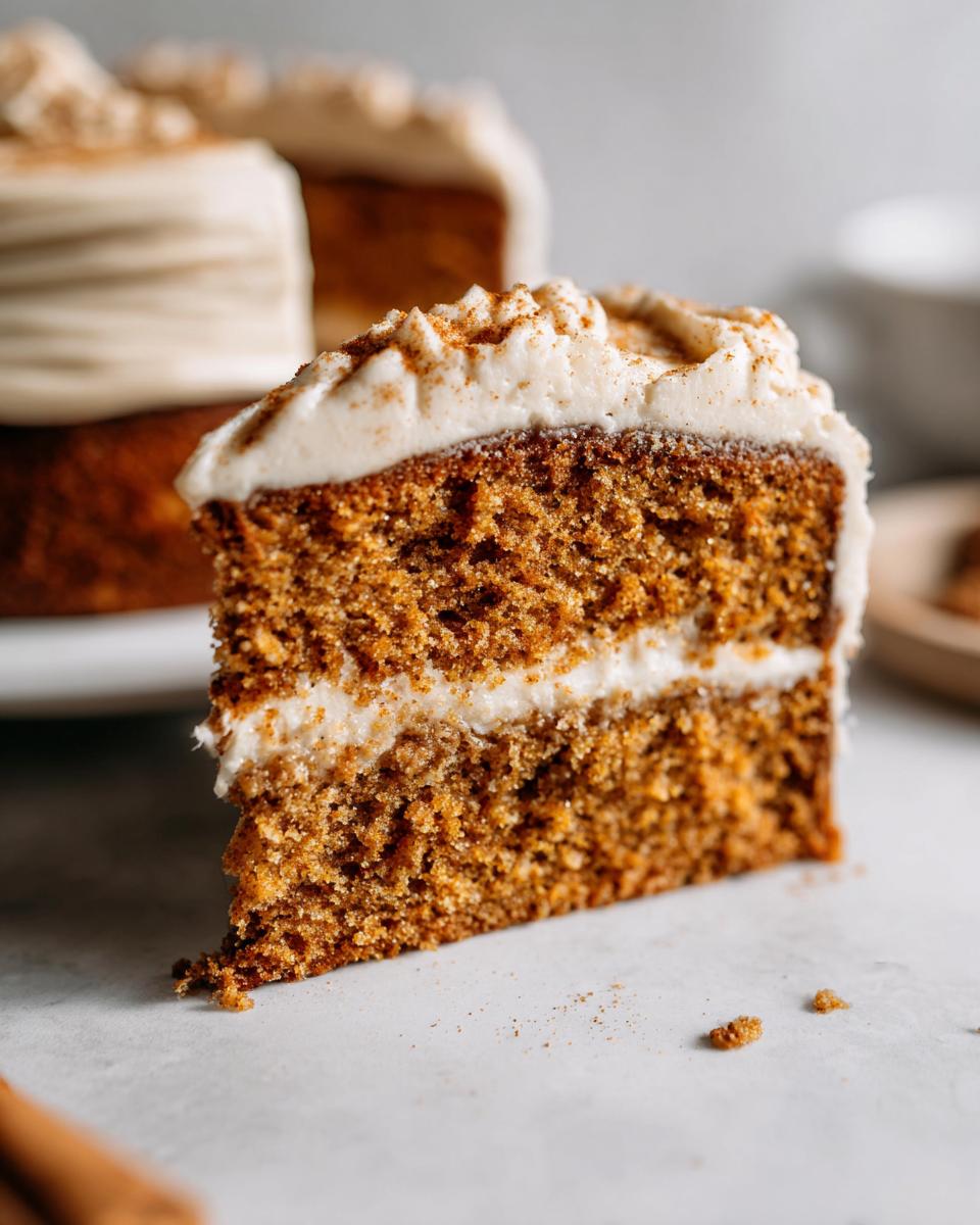 Close-up of a moist slice of Pumpkin Spice Latte Cake showing two layers and thick cream cheese frosting dusted with spice.