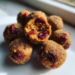 A pile of Raw Gingerbread Cranberry Bites, one is broken open showing dried cranberries inside.