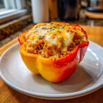 A close-up of a vibrant, baked bell pepper stuffed with Shredded Chicken Rice and topped with melted cheese.
