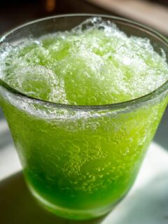 Close-up of a vibrant green, frothy Slime Punch Mocktail filling a clear glass, showing condensation.