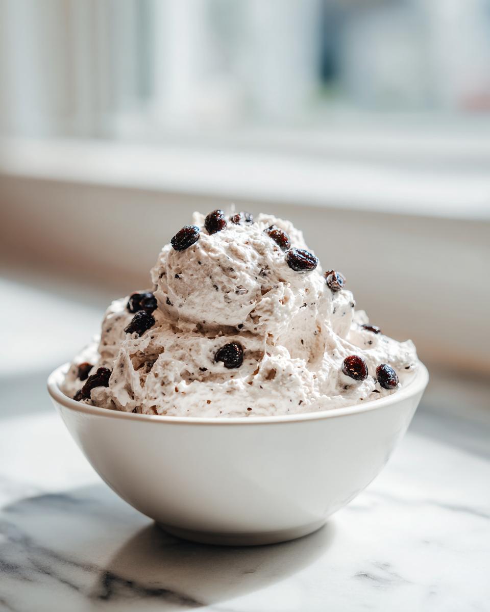 A white bowl filled high with creamy Spider Egg Ranch Dip, topped with dark raisins.