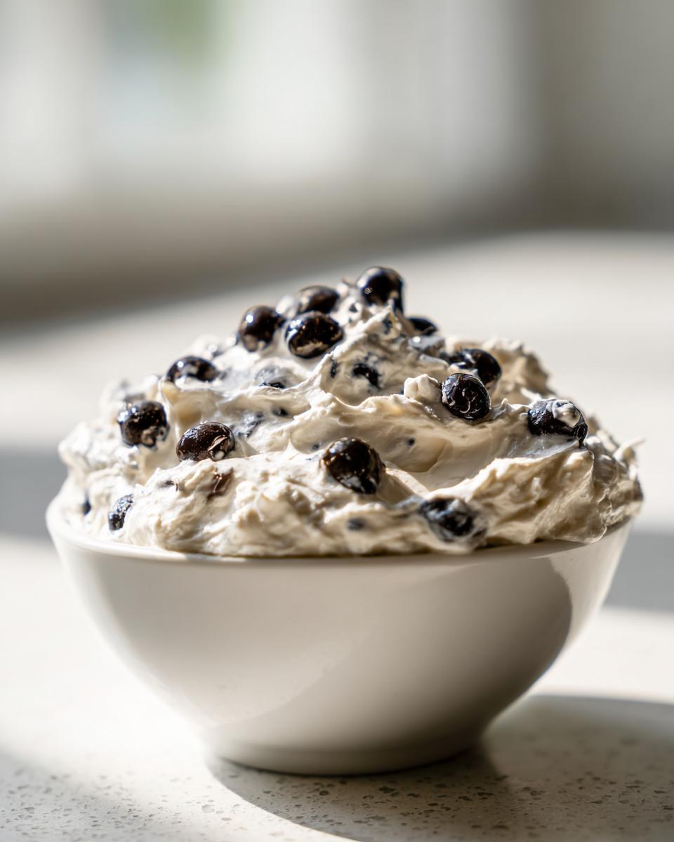 A white bowl filled high with creamy Spider Egg Ranch Dip topped with dark, spherical 'eggs'.