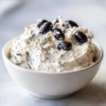 Close-up of rich Spider Egg Ranch Dip topped with whole black olives in a white bowl.