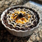 A savory dip decorated like a spiderweb with cheese and a black olive spider for Halloween Dinner Ideas.