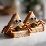 Two Spooky Spider Sandwiches made from triangular bread, pretzel legs, olive heads, and candy eyes.