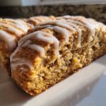 A close-up, angled shot of a freshly baked Starbucks Pumpkin Scones slice topped with thick white icing drizzle.