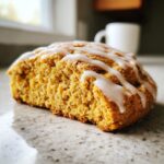 A close-up view of a single, moist Starbucks Pumpkin Scones wedge drizzled with white icing, resting on a granite countertop.