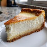 A thick, creamy slice of Sugar Cookie Cheesecake with a golden-brown top and crust.