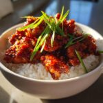 Close-up of crispy Sweet Chili Chicken pieces coated in glaze, served over white rice and topped with fresh green onions.