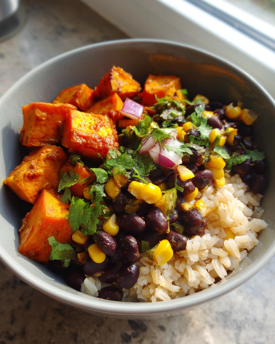 A close-up of a single serving of Sweet Potato Black Bean Bowls featuring brown rice, seasoned black beans, corn, roasted sweet potato cubes, and cilantro.