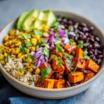 Close-up of a vibrant Sweet Potato Taco Bowl featuring spiced sweet potato cubes, brown rice, black beans, corn, avocado, and red onion.