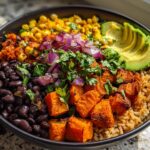 A vibrant Sweet Potato Taco Bowl featuring roasted sweet potatoes, black beans, corn, avocado slices, and red onion over brown rice.