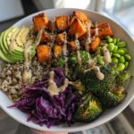 A vibrant Vegan Buddha Bowl featuring roasted sweet potatoes, avocado, quinoa, broccoli, and tahini dressing.