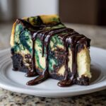A slice of marbled green and brown Witch Cauldron Cheesecake topped with rich chocolate syrup drizzle.