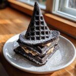 A stack of dark chocolate Witch Hat Waffles dusted with powdered sugar and filled with cream.