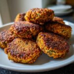 A close-up of a stack of golden-brown, freshly cooked falafel patties on a white plate.
