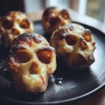 Close-up of four golden-brown, baked Skull Potatoes shaped like human skulls on a black plate.