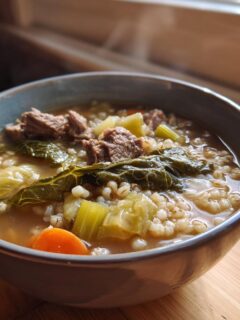 A steaming bowl of hearty Beef Cabbage Barley Soup featuring chunks of beef, barley, carrots, and cabbage.