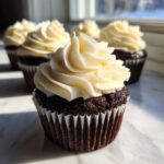 A close-up of a rich, dark chocolate Black Velvet Cupcakes topped with a swirl of creamy white frosting.