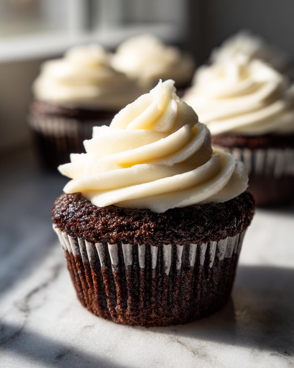 A close-up of one rich, dark Black Velvet Cupcakes topped with a swirl of creamy white frosting.