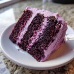 Close-up of a moist slice of Blackberry Velvet Cake showing dark purple layers and light purple blackberry frosting.