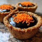 Close-up of a finished Cauldron Cookie Cup with a dark, glossy filling and bright orange sprinkles on top.