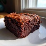 A rich, fudgy square of Chewbacca Brownies with a crackly top, sitting on a white plate near a window.