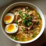 A close-up overhead shot of a bowl of Chicken Miso Ramen topped with shredded chicken, green onions, and two halves of a jammy soft-boiled egg.