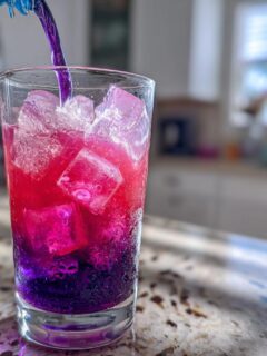 Pouring purple liquid into a glass of ice, causing a dramatic Color Changing Lemonade effect from deep purple to bright pink/red.