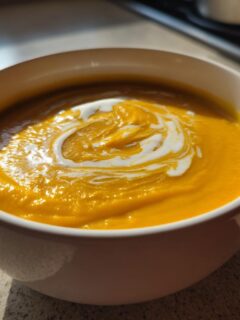 A close-up of creamy, bright orange Acorn Squash Soup topped with a swirl of cream.