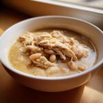 A close-up of a white bowl filled with creamy White Chicken Chili featuring shredded chicken and white beans.