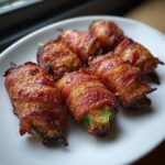 Close-up of six perfectly cooked, crispy bacon-wrapped Jalapeno Mummies served on a white plate.