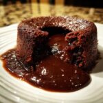 Close-up of a rich Crockpot Chocolate Lava Cake with molten chocolate sauce oozing out onto a white plate.