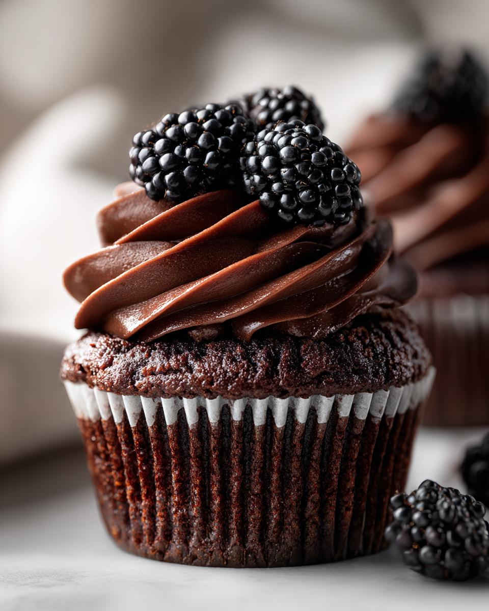 Close-up of a decadent Dark Chocolate Blackberry Cupcakes topped with rich chocolate frosting and fresh blackberries.