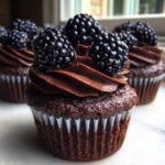 Close-up of a rich Dark Chocolate Blackberry Cupcakes topped with chocolate frosting and fresh blackberries.