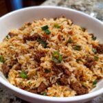 Close-up of a white bowl filled with flavorful Dirty Rice With Ground Beef, garnished with sliced green onions.