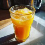 Close-up of a glass filled with bright orange juice, ice cubes, and visible fizz, representing Fizzy Orange Juice.