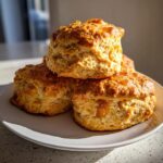 A stack of three golden-brown Ginger Scones, topped with a sweet glaze and visible pieces of candied ginger.