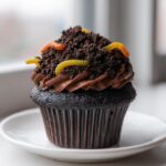 A close-up of a rich Halloween Dirt Cupcakes topped with chocolate frosting, crushed cookie 'dirt', and gummy worms.