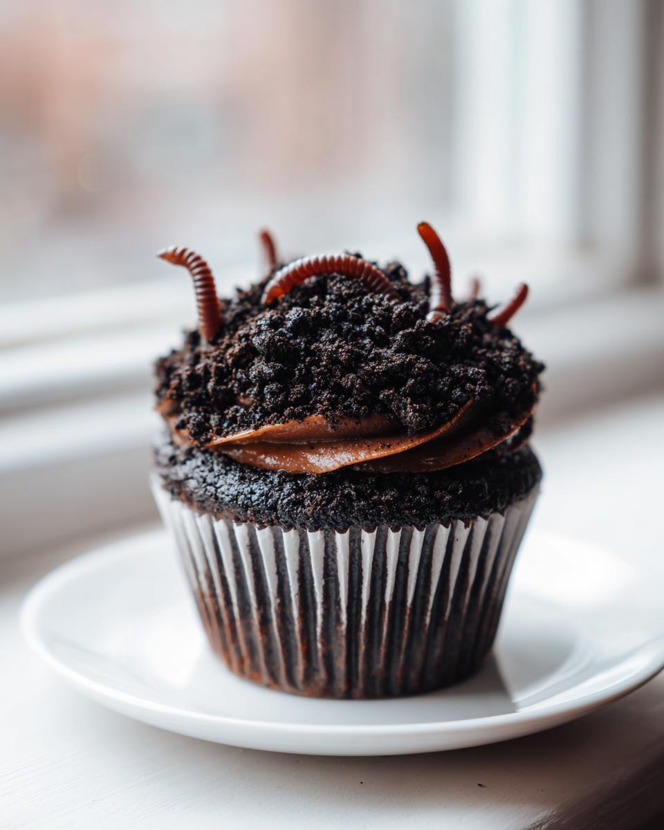 A single, rich chocolate Halloween Dirt Cupcakes topped with crushed cookie 'dirt' and gummy worms emerging from the top.
