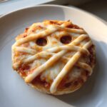 Close-up of a single, baked Halloween Mini Pizzas decorated like a mummy with cheese strips and visible olive eyes.