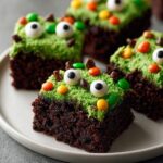 Close-up of rich chocolate Halloween Monster Brownies topped with bright green frosting, candy eyeballs, and colorful candies.