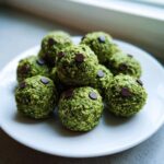 A pile of bright green Halloween Monster Energy Balls, textured with oats, topped with two chocolate chips for eyes.