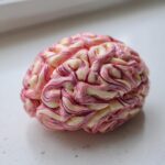 A single, gruesome-looking Halloween Rice Krispie Brains treat with pink and white swirls resembling brain matter, sitting on a white surface.