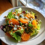 Close-up of a vibrant Halloween Salad featuring mixed greens, bright orange mandarin segments, blue cheese crumbles, and pumpkin seeds.
