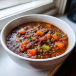 Close-up of a rich, savory bowl of homemade Lentil Stew with visible chunks of carrots and tomatoes.