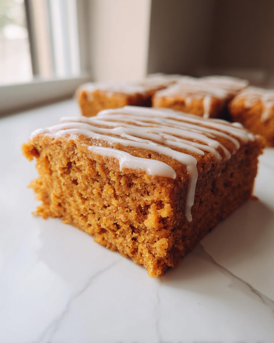 A close-up of a moist, orange-colored Pumpkin Spice Latte Bars square topped with white icing drizzle.